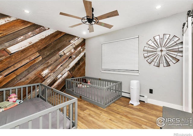 unfurnished bedroom with a baseboard radiator, a barn door, recessed lighting, and wood finished floors