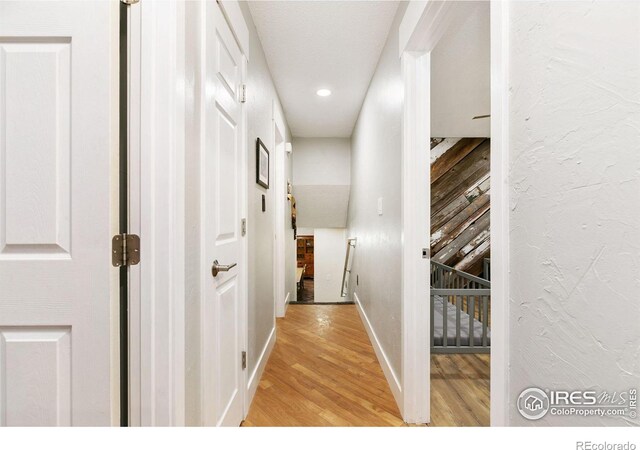 corridor with light wood-type flooring, a textured wall, baseboards, and recessed lighting