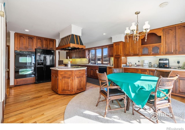 kitchen with a notable chandelier, light countertops, light wood-style flooring, brown cabinetry, and black appliances