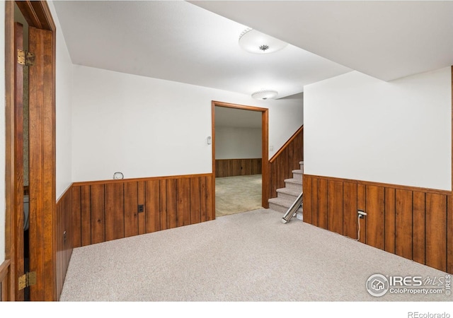 unfurnished room with a wainscoted wall, wooden walls, carpet flooring, and stairs