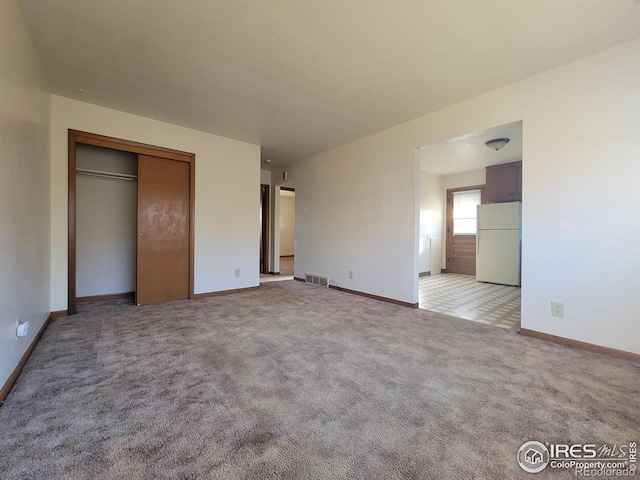 unfurnished bedroom with light carpet, baseboards, visible vents, freestanding refrigerator, and a closet