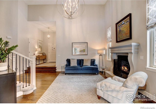 living area featuring a warm lit fireplace, a chandelier, wood finished floors, baseboards, and stairway