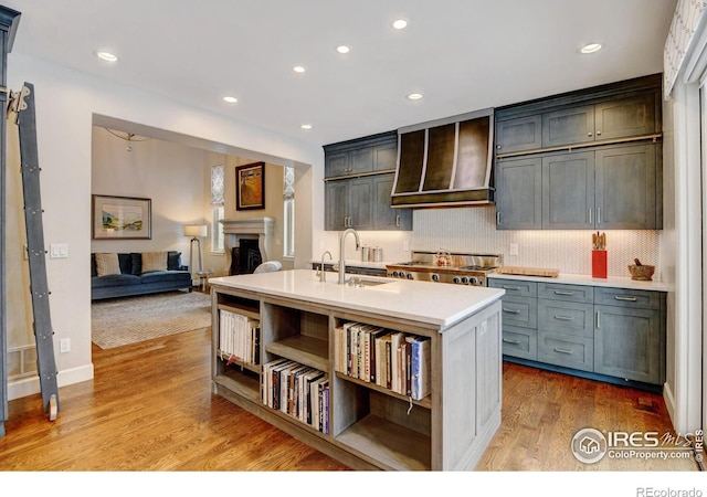 kitchen featuring a fireplace, a sink, light countertops, light wood-type flooring, and custom exhaust hood