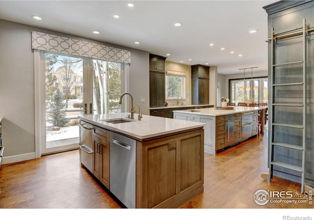 kitchen with dishwasher, a kitchen island with sink, a sink, and wood finished floors