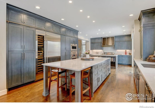 kitchen featuring a spacious island, recessed lighting, custom range hood, wood finished floors, and stainless steel built in refrigerator