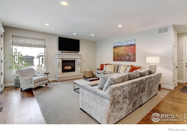 living area featuring recessed lighting, visible vents, a glass covered fireplace, and wood finished floors