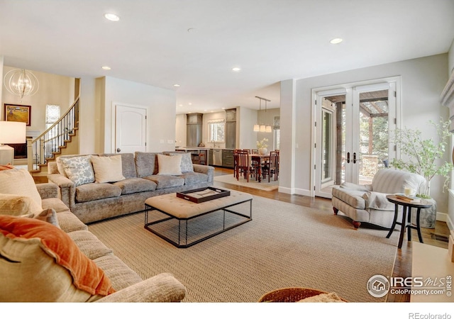 living area with wood finished floors, stairs, french doors, a notable chandelier, and recessed lighting