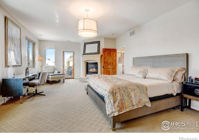 carpeted bedroom featuring a glass covered fireplace and visible vents