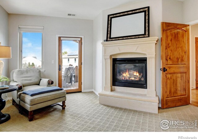 sitting room with carpet floors, a glass covered fireplace, visible vents, and baseboards