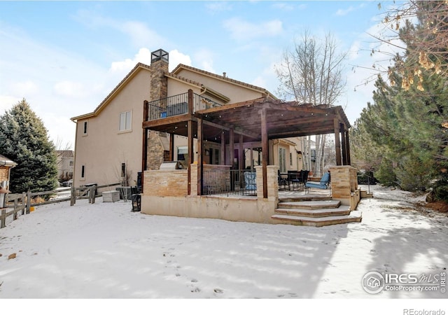 snow covered rear of property featuring a patio area, a chimney, fence, and stucco siding