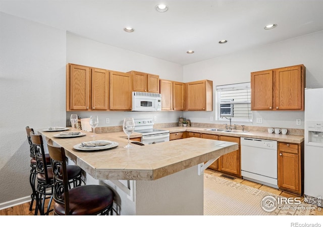 kitchen with white appliances, a peninsula, a kitchen bar, a sink, and recessed lighting