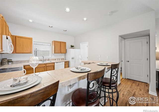 kitchen with tile countertops, recessed lighting, light wood-style floors, white appliances, and a kitchen bar