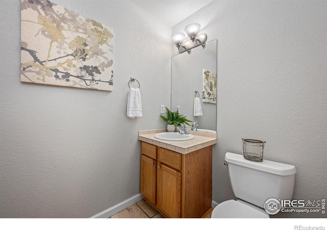 bathroom with toilet, a textured wall, and vanity