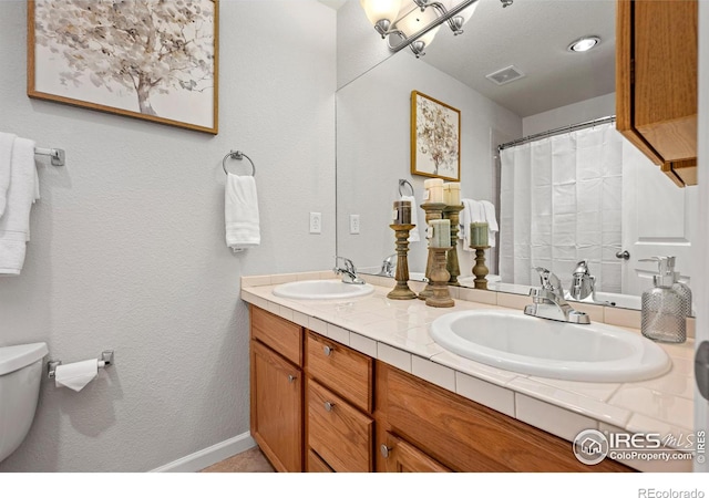 bathroom with visible vents, a sink, toilet, and double vanity