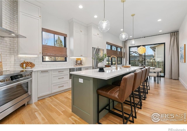 510 Wood St, Fort Collins, CO 80521 - kitchen featuring appliances with stainless steel finishes, wall chimney exhaust hood, decorative backsplash, light countertops, and light wood-style floors