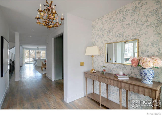 corridor with wallpapered walls, baseboards, a notable chandelier, and wood finished floors