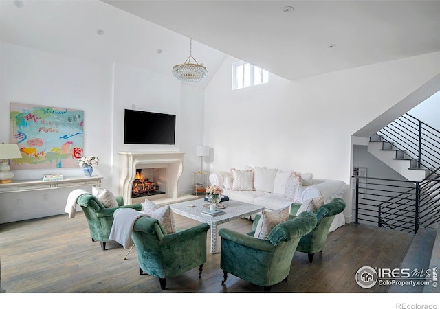 living room with stairs, a warm lit fireplace, a high ceiling, and wood finished floors