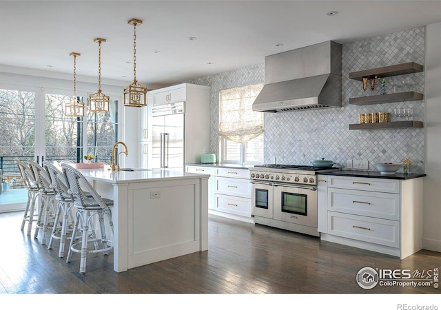 kitchen with white cabinets, wall chimney exhaust hood, high quality appliances, dark wood-type flooring, and a sink