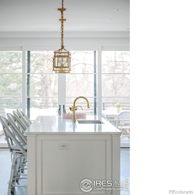 kitchen with a kitchen island with sink, a sink, and hanging light fixtures