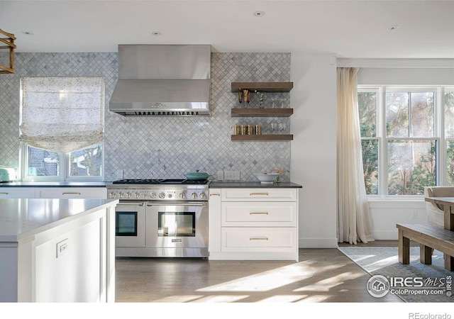 kitchen with backsplash, white cabinetry, wood finished floors, double oven range, and wall chimney exhaust hood