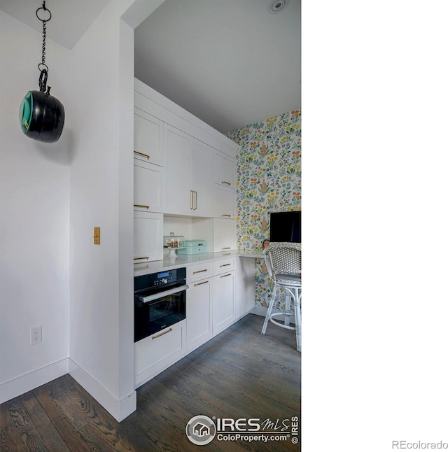 kitchen featuring wall oven, wallpapered walls, white cabinets, dark wood-style flooring, and light countertops