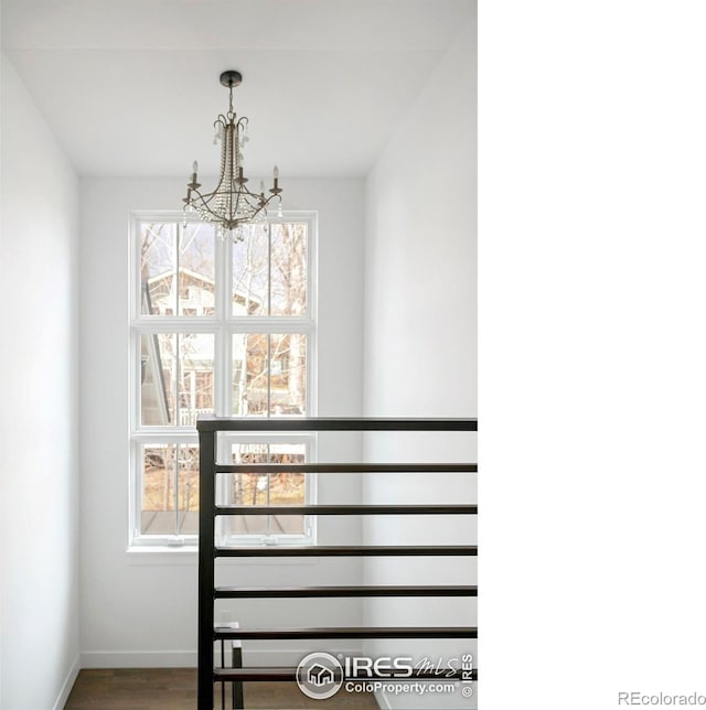 staircase with baseboards, plenty of natural light, an inviting chandelier, and wood finished floors