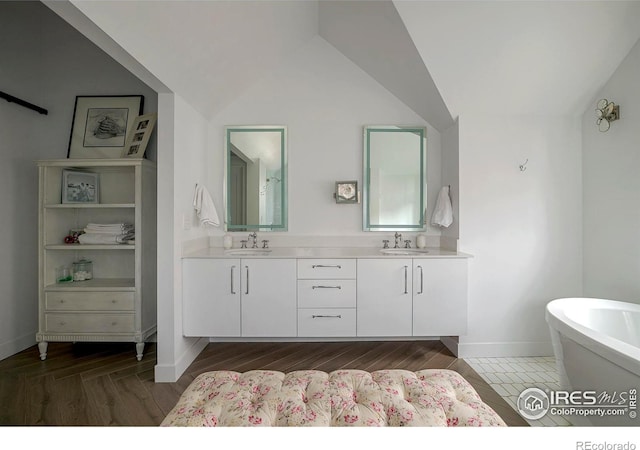 bathroom featuring a soaking tub, vaulted ceiling, a sink, and double vanity