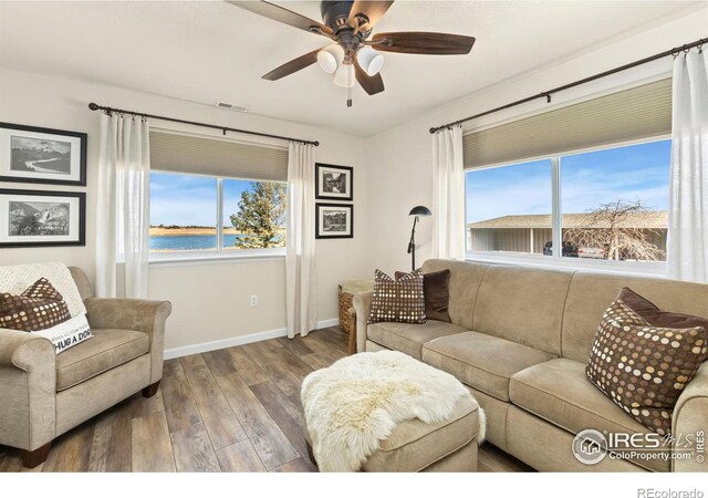 living room with a water view, wood finished floors, visible vents, a ceiling fan, and baseboards