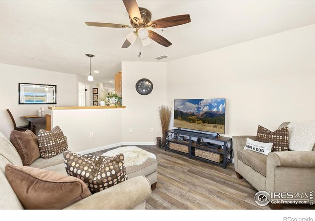 living room with a ceiling fan, visible vents, baseboards, and wood finished floors