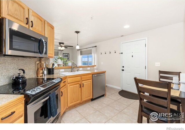 kitchen featuring light tile patterned flooring, stainless steel appliances, a peninsula, a sink, and tasteful backsplash