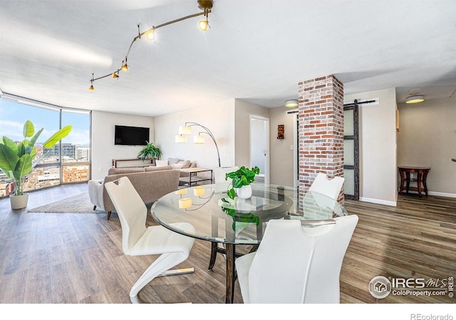 dining space featuring a barn door, track lighting, wood finished floors, a wall of windows, and baseboards