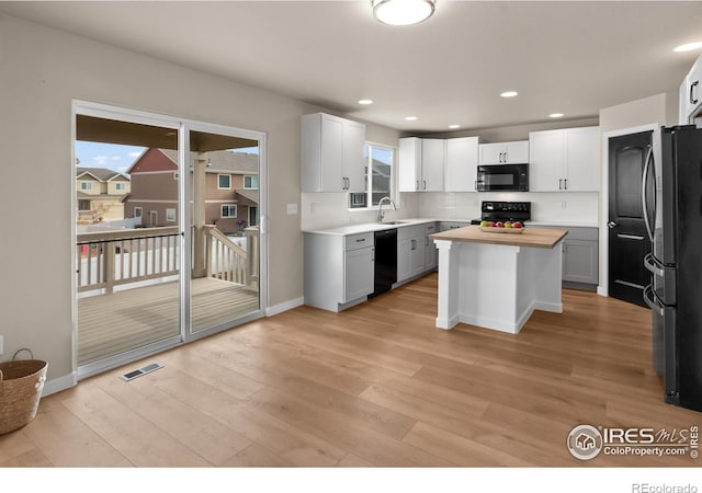 kitchen with visible vents, black appliances, light wood-style flooring, a sink, and a center island