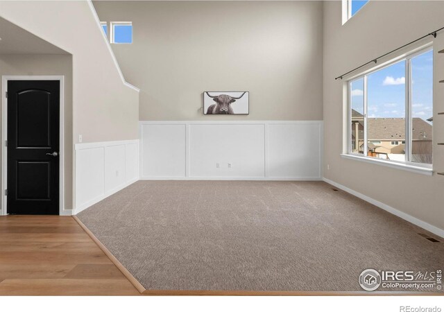 unfurnished room with carpet, wood finished floors, visible vents, wainscoting, and a decorative wall