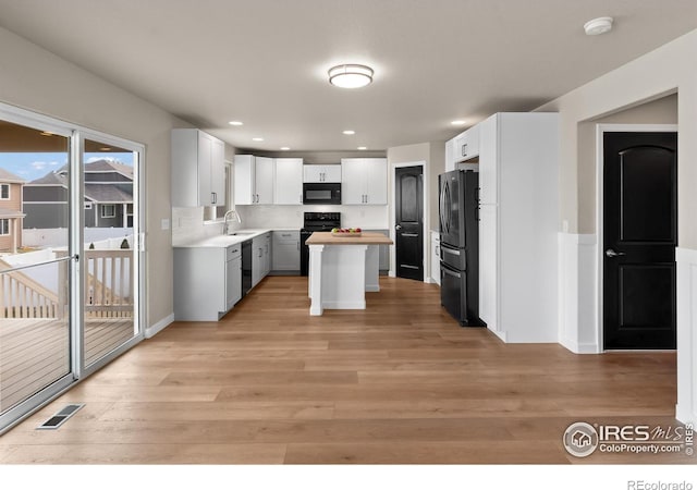 kitchen with visible vents, light wood finished floors, a sink, butcher block countertops, and black appliances