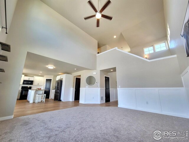 unfurnished living room featuring ceiling fan, light carpet, recessed lighting, wainscoting, and a high ceiling