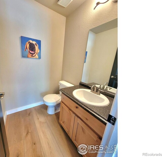 half bathroom featuring vanity, wood finished floors, visible vents, baseboards, and toilet