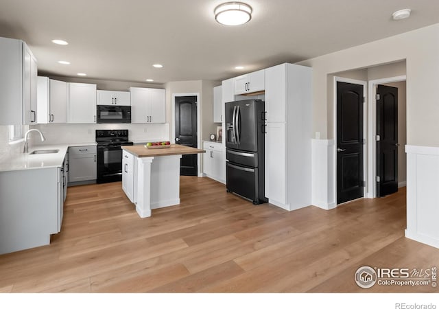 kitchen with black appliances, light wood-style flooring, a sink, a center island, and white cabinets