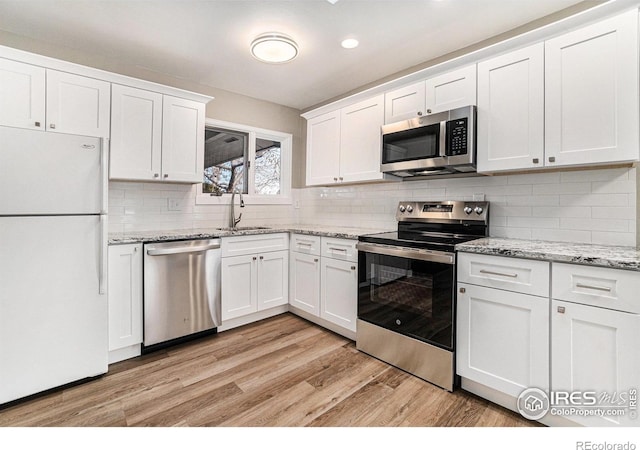 kitchen featuring stainless steel appliances, backsplash, light wood-style flooring, white cabinets, and a sink