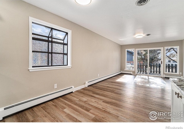 spare room featuring a baseboard heating unit, a baseboard radiator, visible vents, and wood finished floors