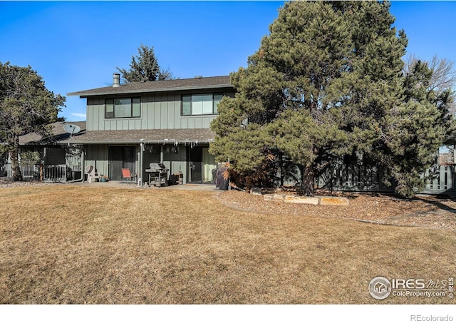 rear view of house featuring board and batten siding, fence, and a lawn