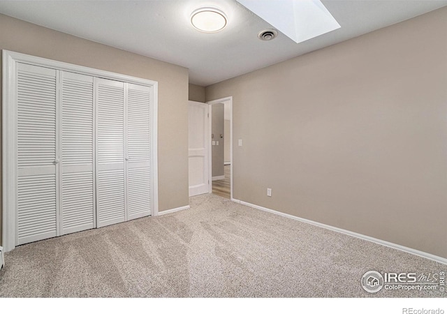 unfurnished bedroom featuring a skylight, visible vents, baseboards, carpet, and a closet