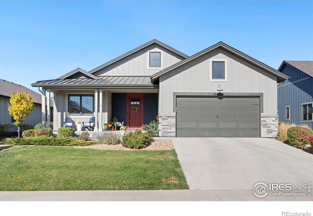 modern farmhouse featuring concrete driveway, an attached garage, a standing seam roof, covered porch, and a front yard