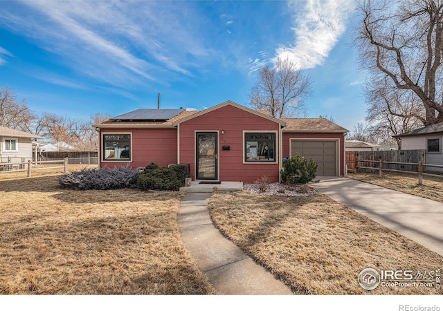 view of front of property with a garage, driveway, fence, roof mounted solar panels, and a front lawn