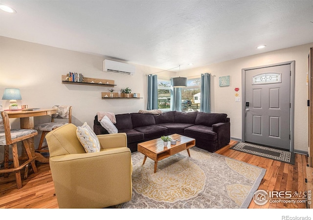 living area with a textured ceiling, a wall unit AC, wood finished floors, and recessed lighting