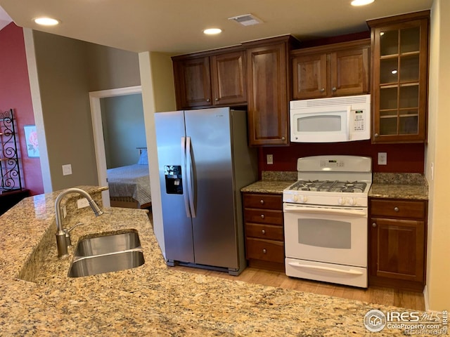 kitchen featuring visible vents, glass insert cabinets, a sink, light wood-type flooring, and white appliances