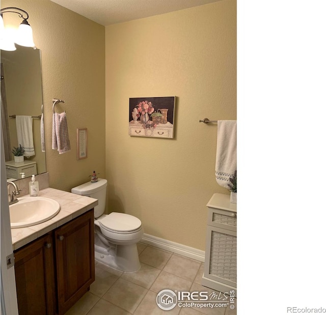 half bath with toilet, tile patterned flooring, baseboards, and vanity