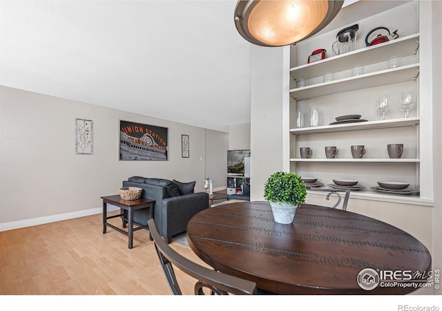 dining space with built in features, baseboards, and light wood finished floors