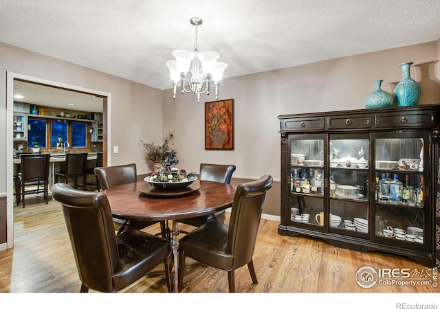 dining room with a chandelier, a textured ceiling, baseboards, and light wood-style floors