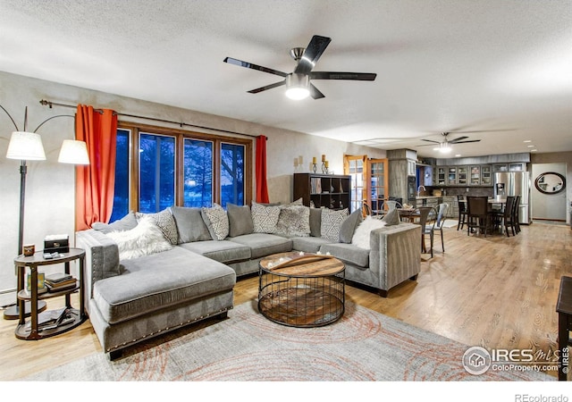 living area with ceiling fan, a textured ceiling, and wood finished floors