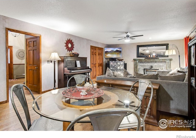 dining area with a fireplace, a baseboard heating unit, ceiling fan, a textured ceiling, and wood finished floors